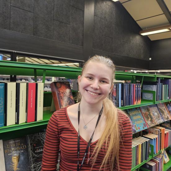 Portræt af Anne Asaa med bibliotek i baggrunden. Hun er tovholder for læseklubben ”Læsepiloterne” på Odder Bibliotek